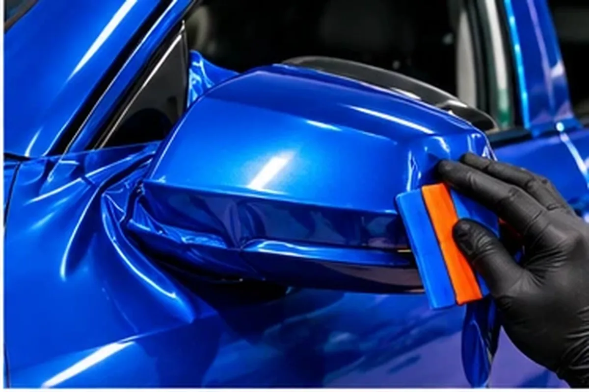 Installer applying bright blue vinyl with an orange squeegee